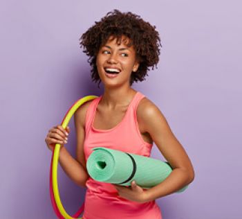 A woman smiling holding a yoga mat and hoops