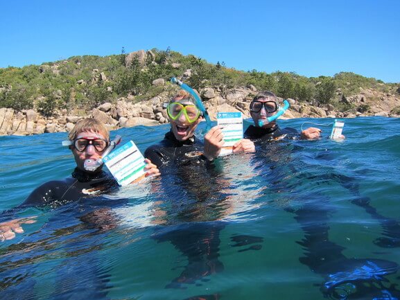 Photo credit: Tourism and Events Queensland Three men snorkelling and holding checklists
