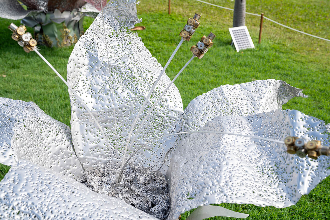 Three ethereal flowers created from recycled aluminium and copper, recycled shotgun shells, and brass casings
