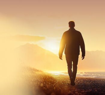 Man walking on a beach at sunset with mountains in the background